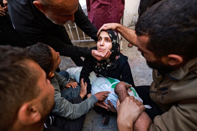 People try to comfort a woman holding the body of her baby girl killed in an Israeli strike in Rafah in the southern Gaza Strip in the courtyard of the al-Najjar hospital on Dec. 1, 2023.
