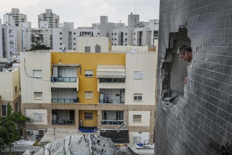 A man looks through a hole in the wall of a house as a result of rockets fired from the Gaza Strip, in Ashkelon, Israel, Tuesday, Dec. 5, 2023. 