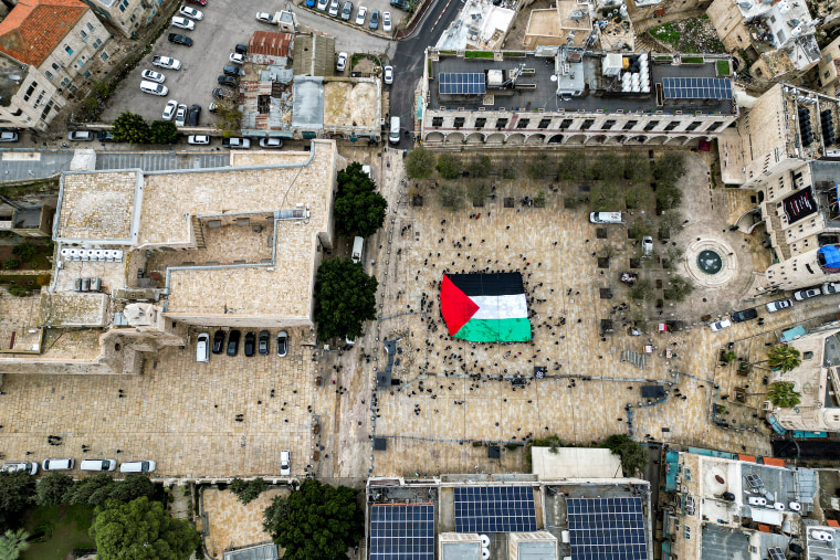 A Palestinian flag is unfurled as people gather at the Manger Square in Bethlehem on Christmas Eve. 