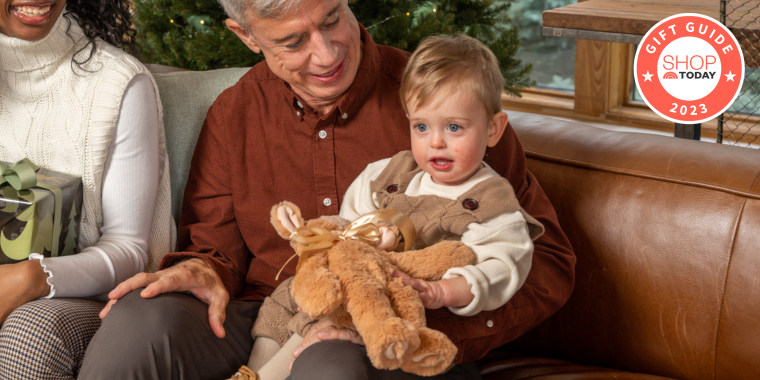 1 year old holding a stocking stuffer while sitting on his dad's lap.