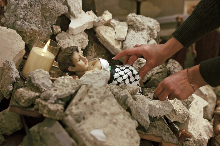 A woman arranges a nativity scene with baby Jesus surrounded by rubble at the Evangelical Lutheran Church in Bethlehem in the occupied West Bank on Dec. 6, 2023.