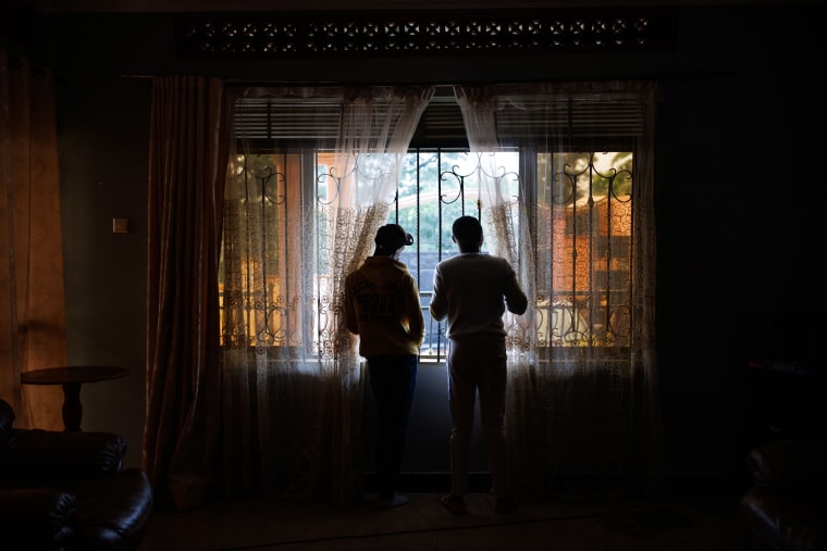 Two shadowed people look out of window , while adjusting curtains
