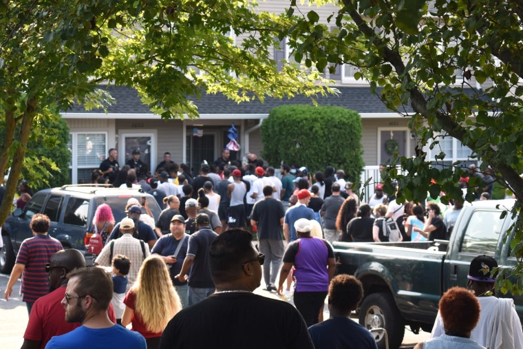 A crowd forms in front of the house of Edward Mathews, which is blocked by police.