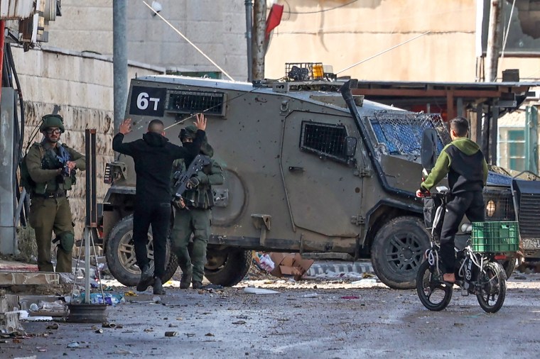 An Israeli soldier on patrol checks a Palestinian youth on Dec. 13, 2023, following an overnight army raid in Jenin in the occupied West Bank.