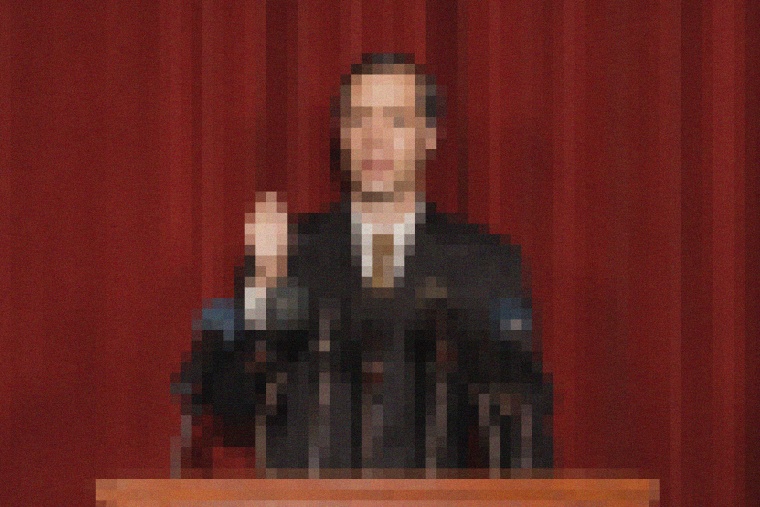 Image:  A pixelated politician speaks at a podium of microphones.
