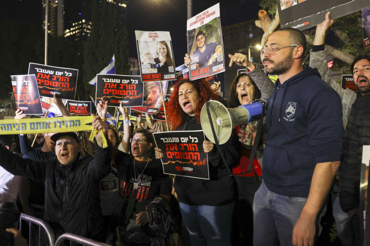 People hold sign, some with images of Israeli hostages, while protesting.