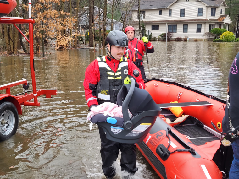 Firefighter and Police Sgt. Matthew Buesser rescues a baby after the family’s home was hit by floods Monday.