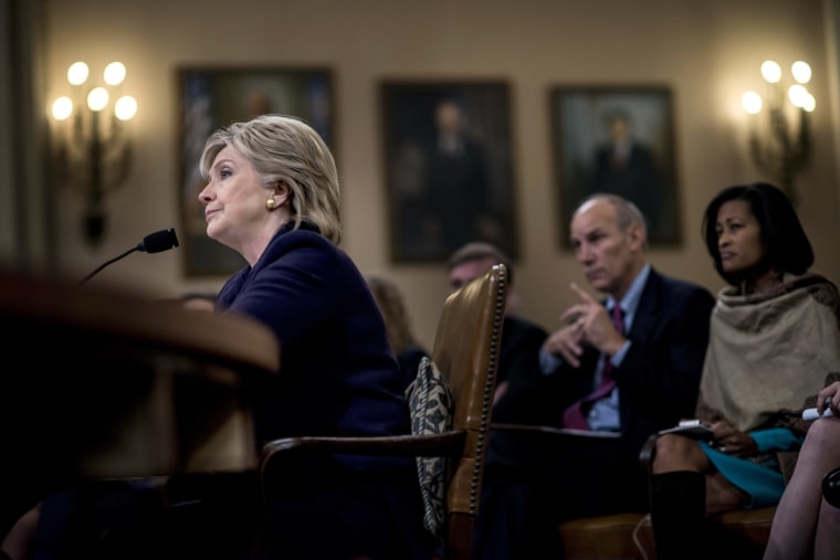 Former Secretary of State Hillary Clinton sits at a table with audience members behind her.