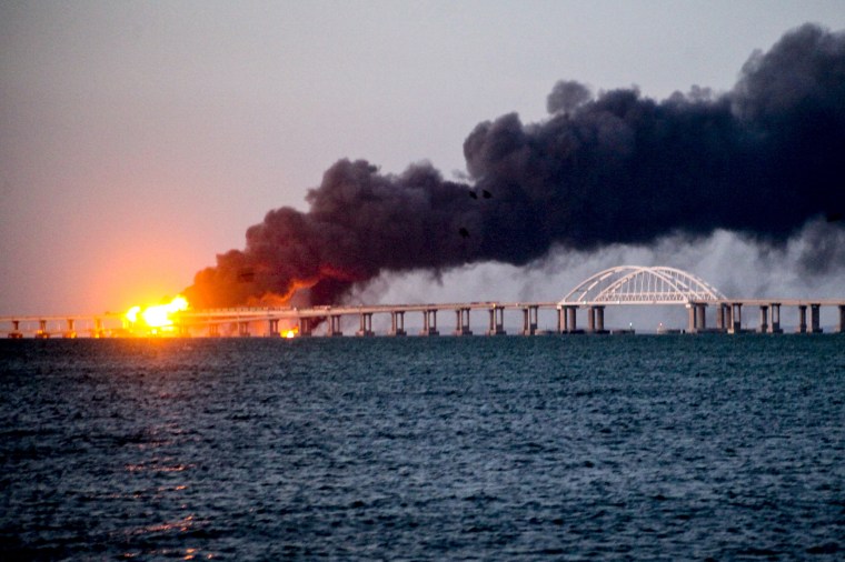 A wide angle photo of the Kerch bridge on fire and smoke billowing.
