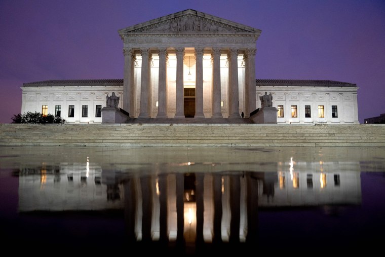 The US Supreme Court is reflected in a puddle of water at night.