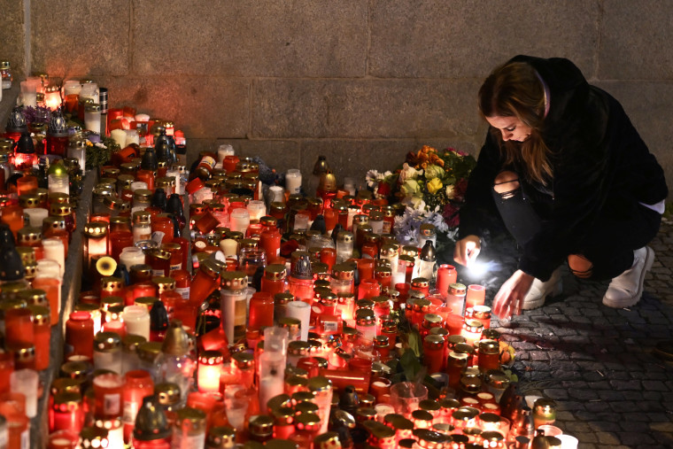 A person kneels to light a candle at a memorial.
