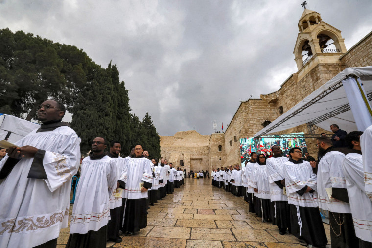 Clergymen wait ahead of Christmas service in the Manger Square outside the Church of the Nativity in Bethlehem