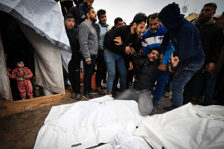 Displaced Palestinian children watch from inside a tent as a man mourns relatives.