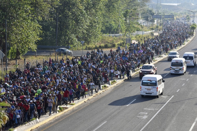 A large crowd of migrants march along a highway.