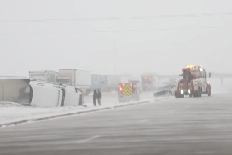 Emergency crews examine a flipped over freight truck on a snowy interstate.