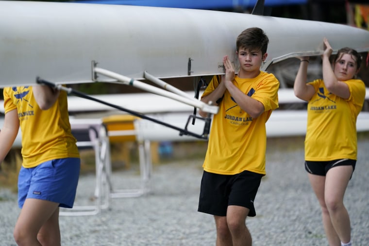 Callum Bradford, center, and his team, carry their boat to the ramp as they get ready for a rowing club practice at Jordan Lake, in Apex, N.C.
