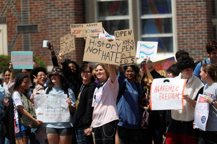 Students holds signs that read, "History not hate," "Academic freedom," and "We are the Future" along with other signs with the transgender flag.