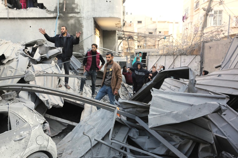 People stand on top of the rubble of a destroyed structure.