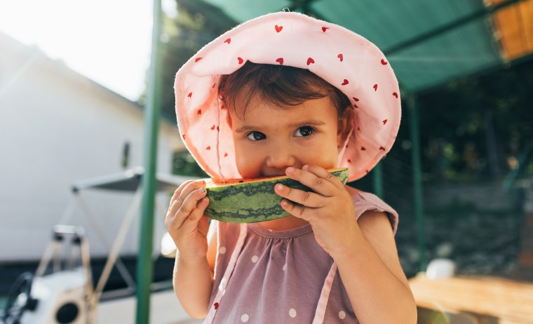 A Cute Baby Girl Eating Watermelon While Standing Outdoors