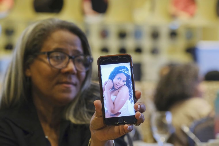 A woman holds a phone with a picture of her daughter.