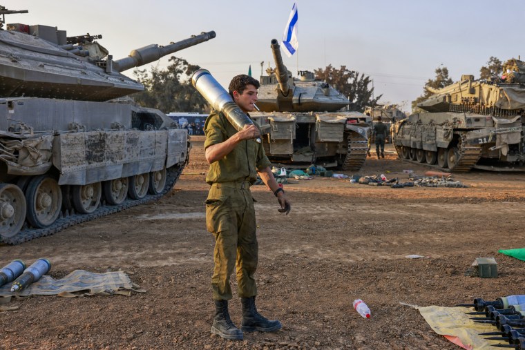 An Israeli soldier carries a heavy shell past battle tanks deployed at a position along the border with the Gaza Strip and southern Israel on Dec. 31, 2023.