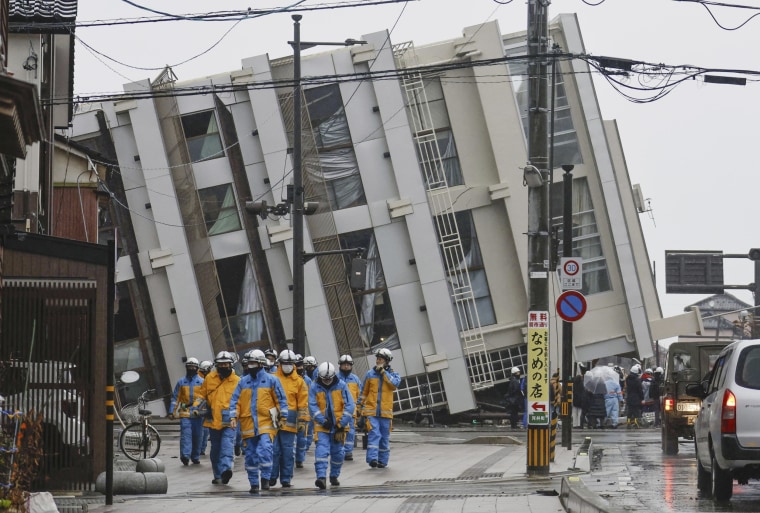 Firefighters walk near a fallen building following earthquakes in Wajima, Ishikawa prefecture, Japan Wednesday, Jan. 3, 2024. 