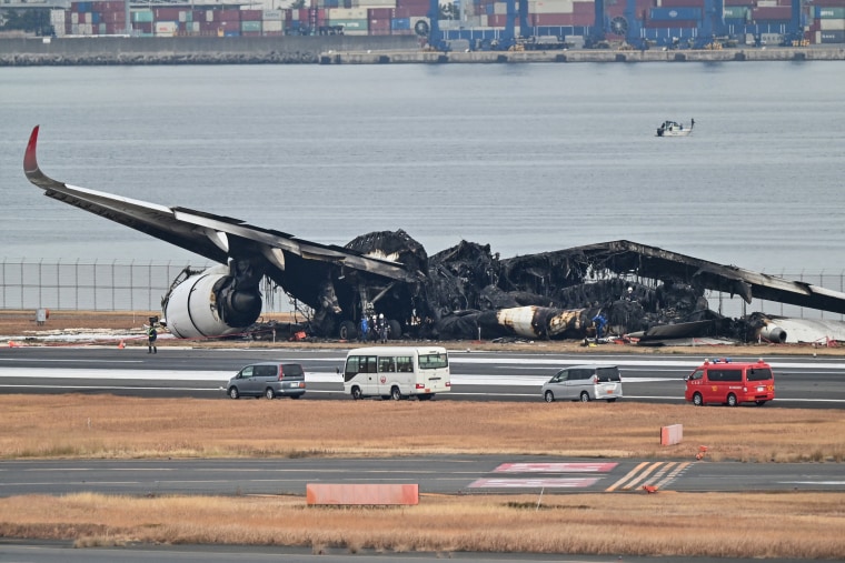 Officials look at the burned wreckage of a Japan Airlines passenger plane on the tarmac at Tokyo International Airport at Haneda in Tokyo on Jan. 3, 2024, the morning after the JAL airliner hit a smaller coast guard plane on the ground. 