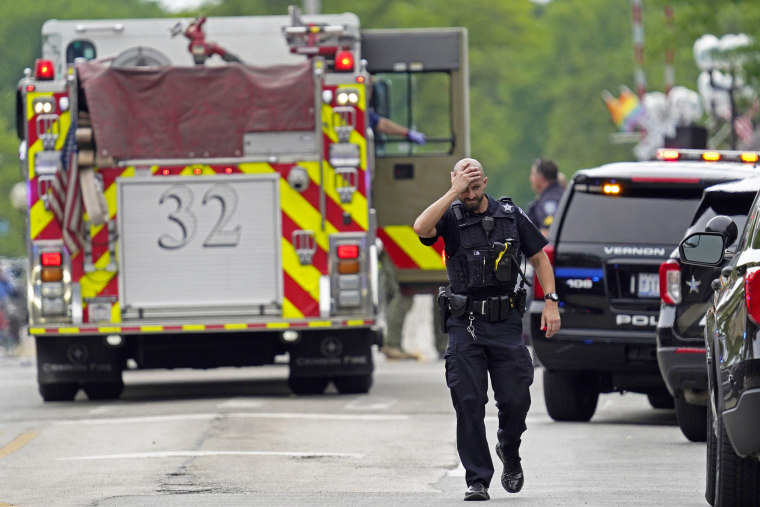 A police officer walks down the street among emergency vehicles.