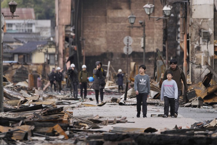 People walk through debris after a fire at a shopping area in Wajima in the Noto peninsula, facing the Sea of Japan, northwest of Tokyo, Friday, Jan. 5, 2024, following Monday's deadly earthquake. 
