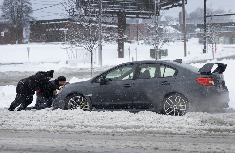 People help push a vehicle back onto the road after it became stuck in the snow in Des Moines, Iowa, today.