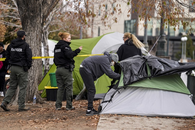 A man collects items from a tent as Denver Parks Department rangers remove police tape during a city-sponsored camp cleanup