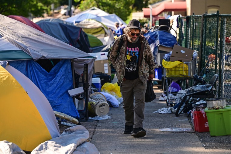 An unhoused man walks with his belongings at the encampment along North Logan street and E. Eighth ave 