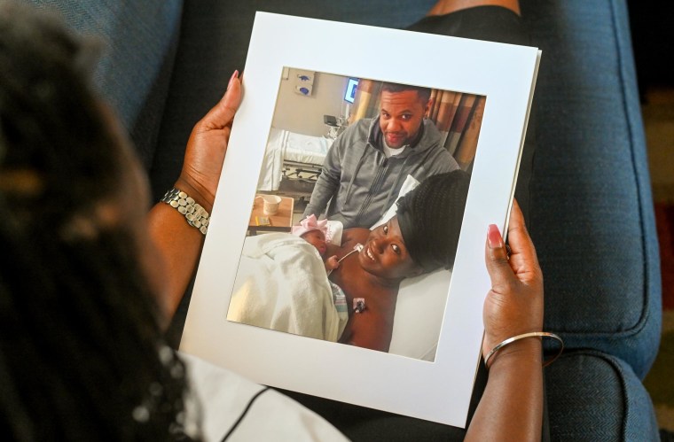 Image: Charity Watkins holds a photo of her, her newborn daughter and her husband.