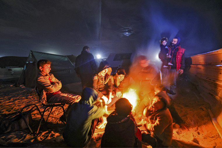 Displaced Palestinians warm by the fire at a makeshift camp west of Rafah near the Egyptian border on Jan. 14, 2024.