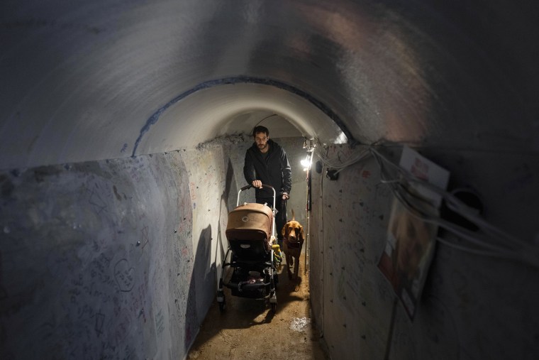 An Israeli man pushes his baby stroller and walks his dog through an installation in Tel Aviv that simulates a tunnel in Gaza on Jan. 14, 2024. 