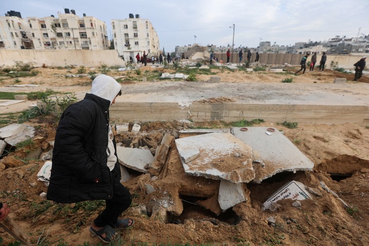 Palestinians check damaged graves at a cemetery following an Israeli raid, in Khan Younis