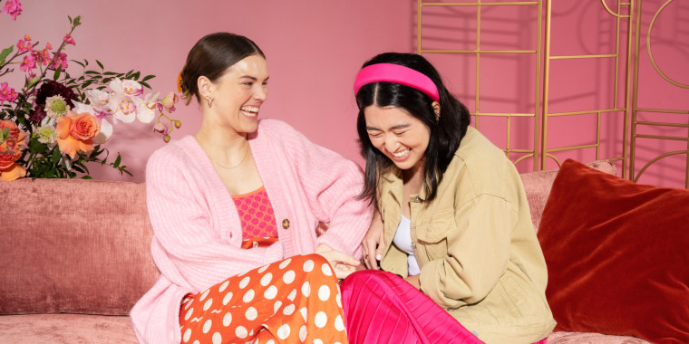 two women laughing while sitting on a sofa