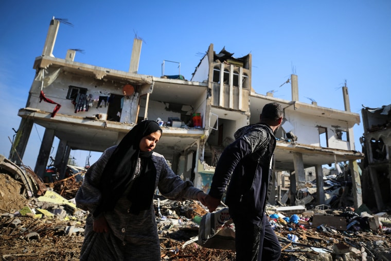 Image: Palestinian people walk past a destroyed building in the Al-Maghazi refugee camp