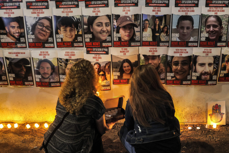 People light candles beneath a wall showing posters identifying hostages abducted by Palestinian militants during the October 7 attack, in Jerualem