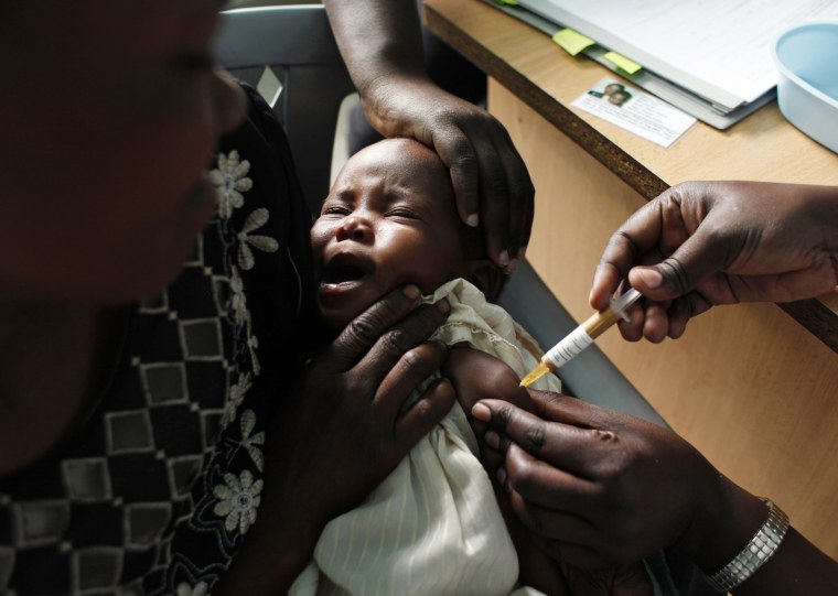 A mother holds her baby receiving a malaria vaccine in Kombewa, Kenya