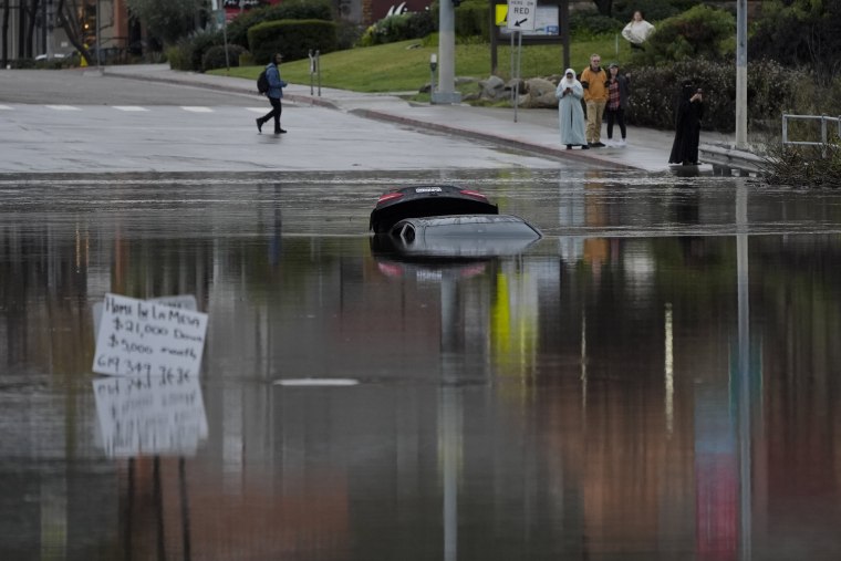 A car sits partially submerged on a flooded road during a rain storm, in San Diego