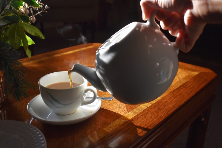 Pouring hot tea into a cup on wooden table background, Traditional english tea