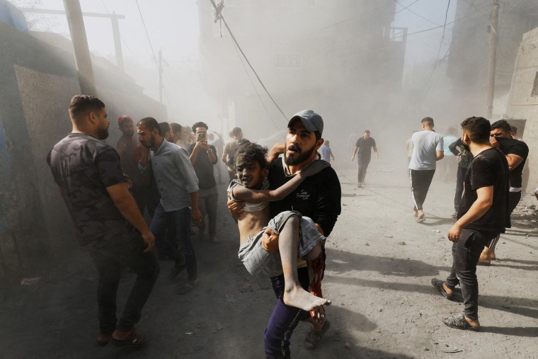 A Palestinian man carries a child casualty at the site of Israeli strikes on houses, in Khan Younis