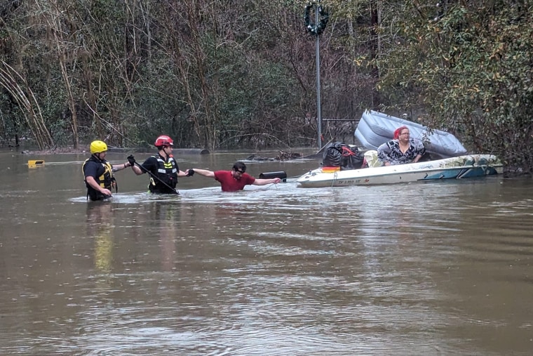 Emergency Service workers hold a man's hands in the San Jacinto River while another evacuee sits on a small boat. 