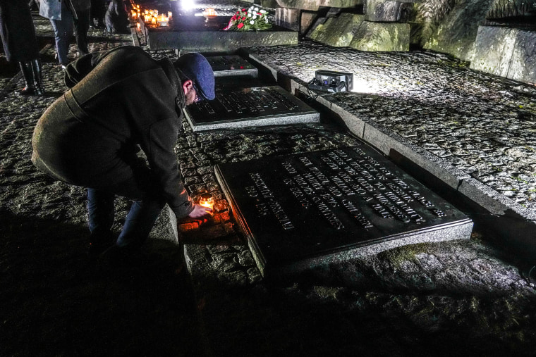 Image: A man places a candle next to the monument at the Birkenau Nazi death camp