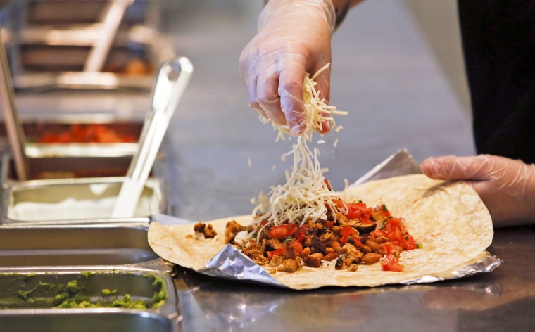 A employee sprinkles cheese on a burrito at a Chipotle.