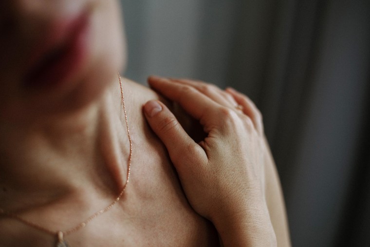 Close-up photo of unrecognizable naked woman with hand delicately resting on shoulder