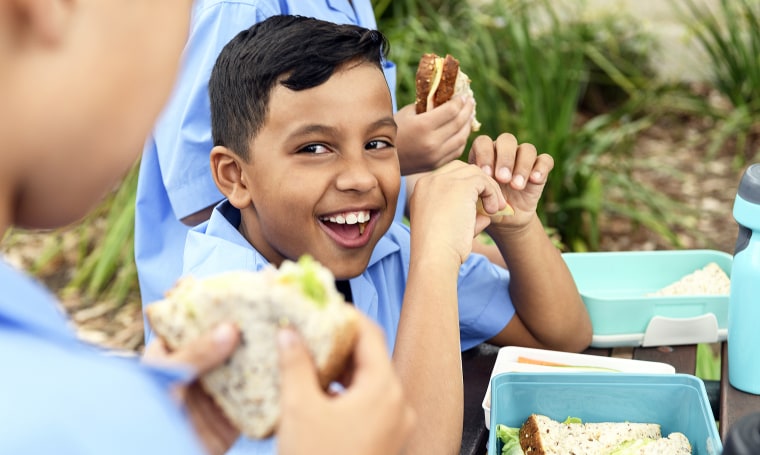 Young school boy smiling while eating lunch