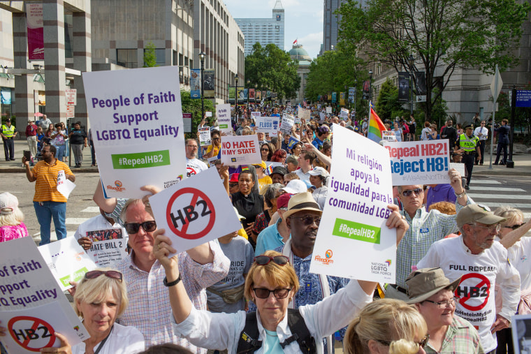 Protesters hold signs that read, "People of Fait Support LGBTQ Equality. Repeal HB2. 