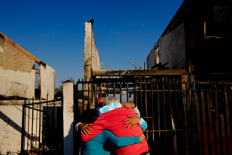 Residents hug in front of a burnt home.